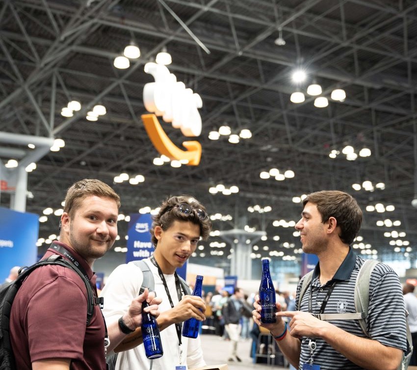 Three guys cheersing water bottles under an AWS sign